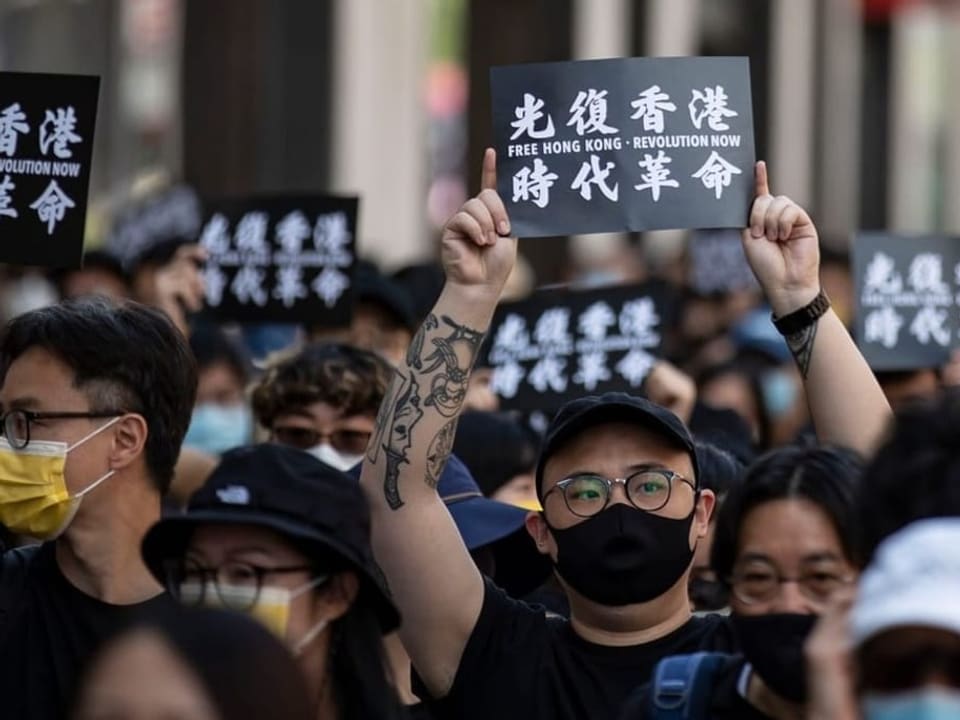 Menschenmasse mit Gesichtsmasken hält schwarze Protestschilder hoch mit chinesischen Schriftzeichen