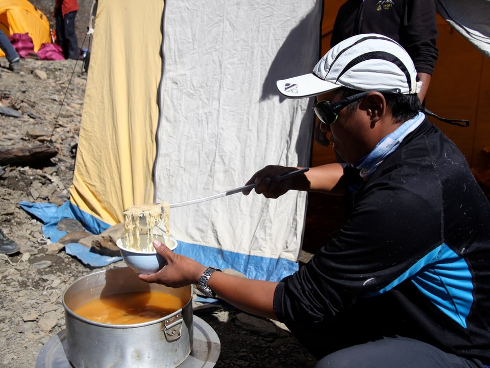 Ein Sherpa schöpft Nudelsuppe aus einem grossen Topf.