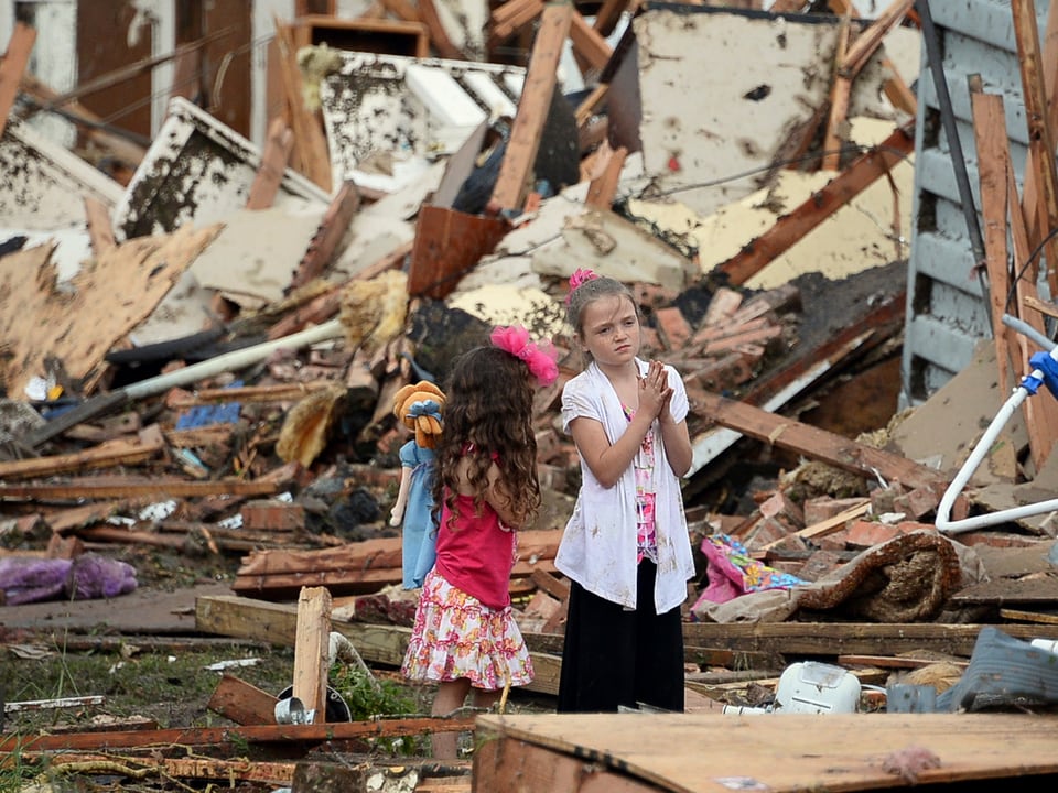 Zwei Kinder vor Trümmern. Eines der Mädchen hält die Hände zum Gebet.