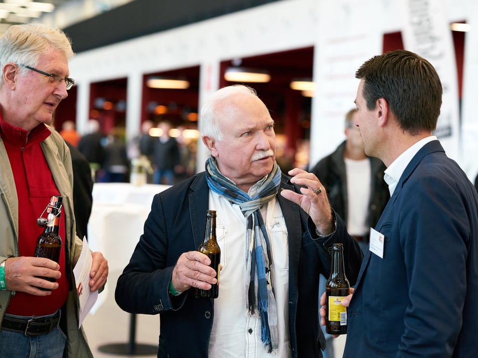 Drei Mannen im Gespräch, jeder mit einer Bierflasche in der Hand. 