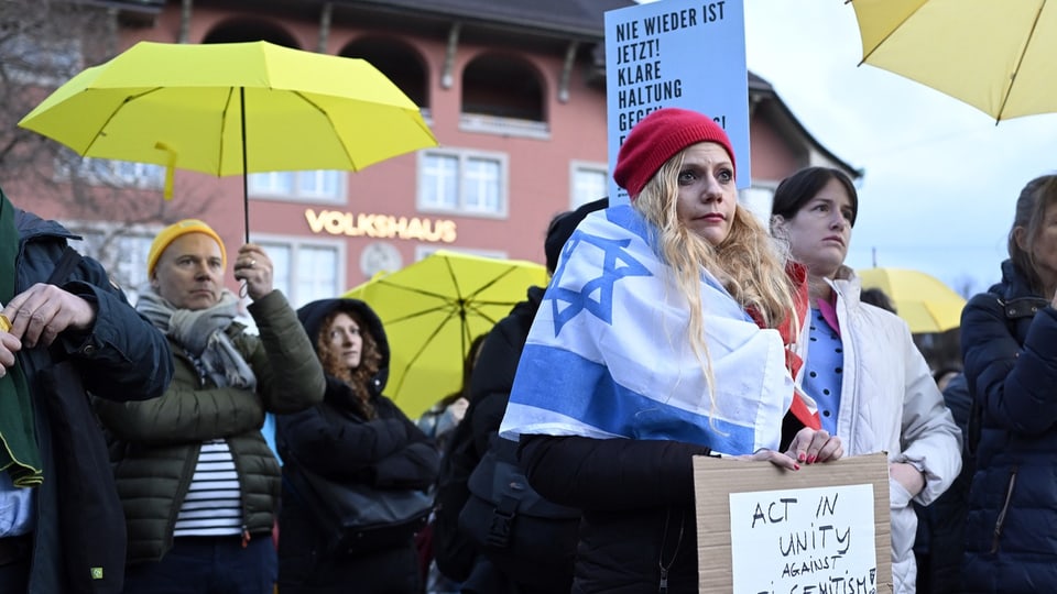 Demonstranten mit Regenschirmen und Plakaten gegen Antisemitismus