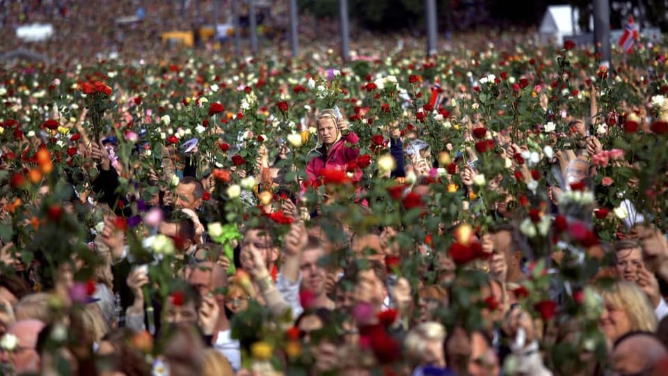 Eine grosse Menschenmenge steht dicht nebeneinander und hält Rosen in die Luft.