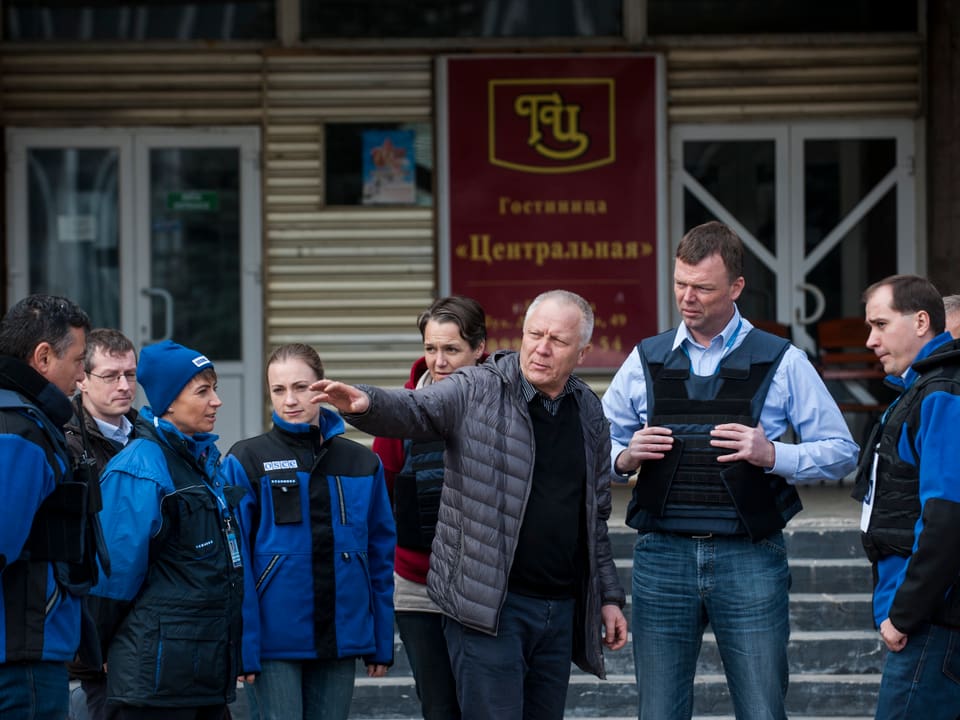Ein Zivilist spricht mit einer Gruppe Personen in blauen OSZE-Uniformen.