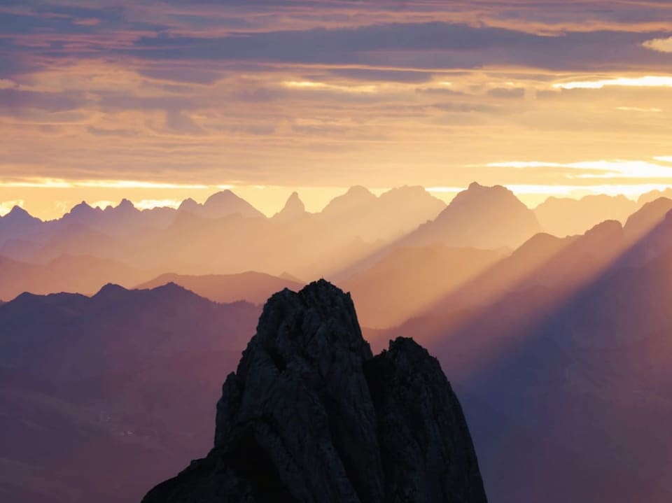Schwarzer Fels im Vordergrund, Hintergrund Berge und Täler im Dunst und Morgenlicht.