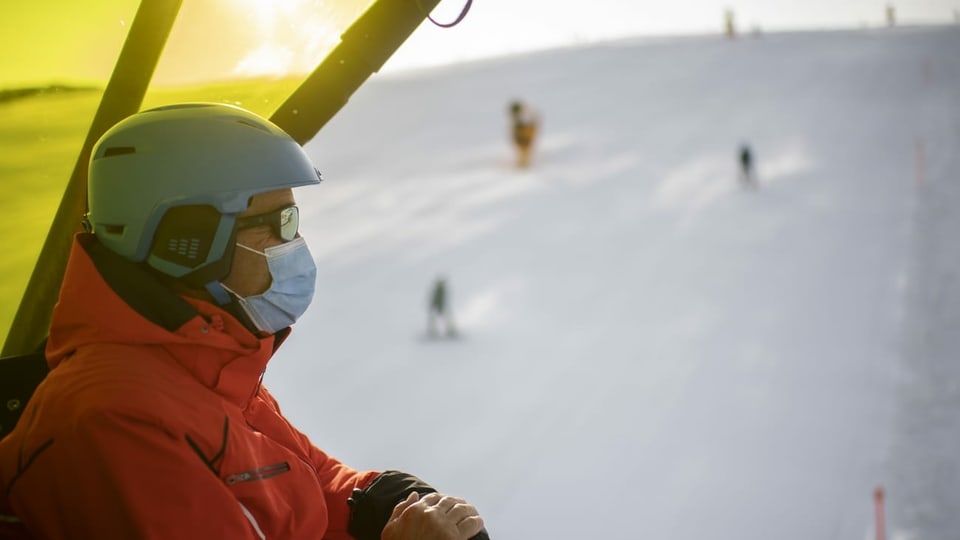 Skifahrer mit Gesichtsmaske auf einem Sessellift.