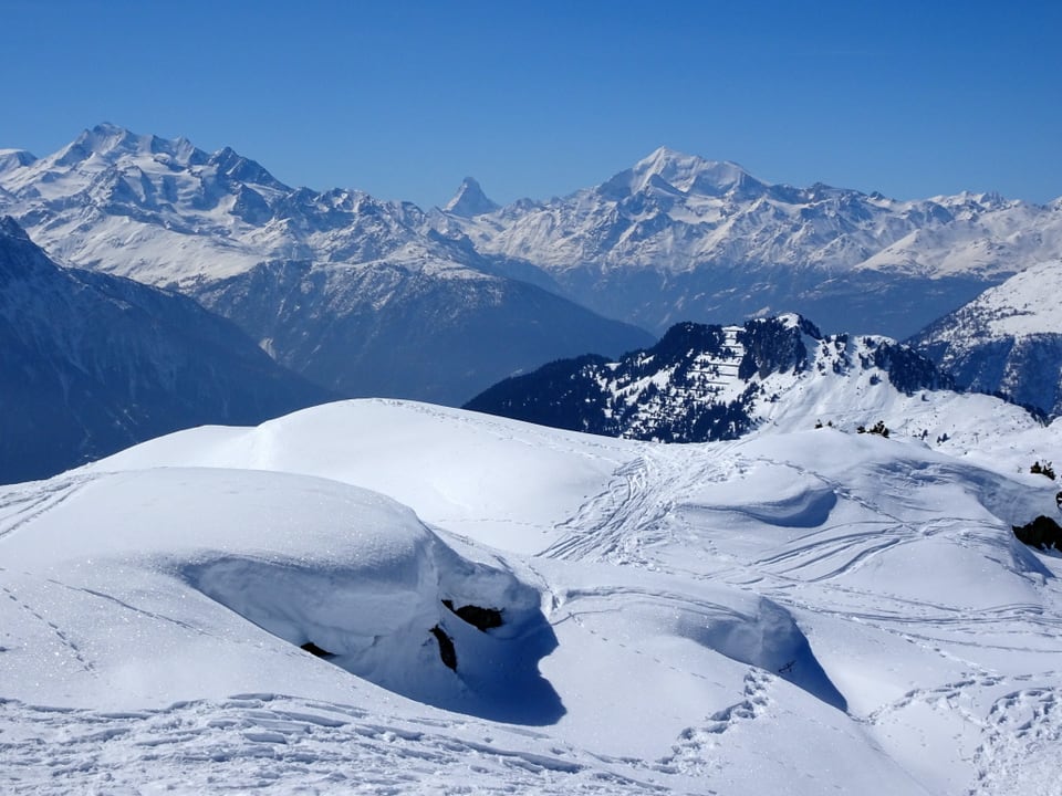 Schneelandschaft, im Hintergrund Bergpanorama mit blauem Himmel.