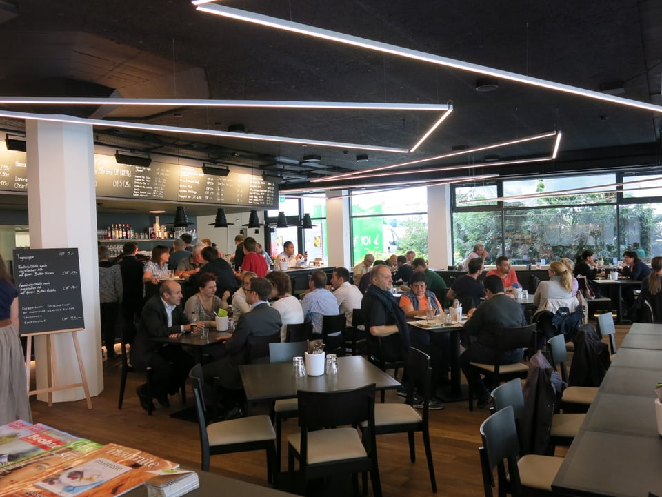 Ein Restaurant mit schwarzer Möblierung und viele Leute, die sitzen.