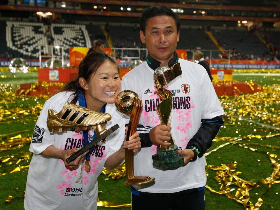Eine Japanerin posiert mit einem goldenen Fussball und einem goldenen Pokal.