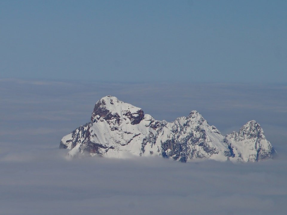 Nebelmeer mit einsamer Bergspitze, die herausragt. Darauf hat es Schnee. Über dem Nebel scheint die Sonne. 