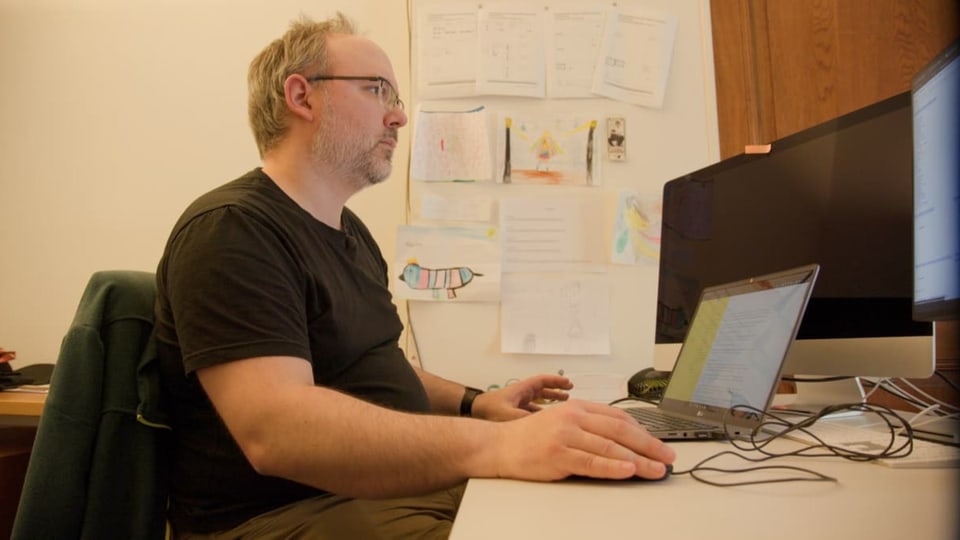 Mann mit schwarzem T-Shirt und Brille arbeitet an einem Computer