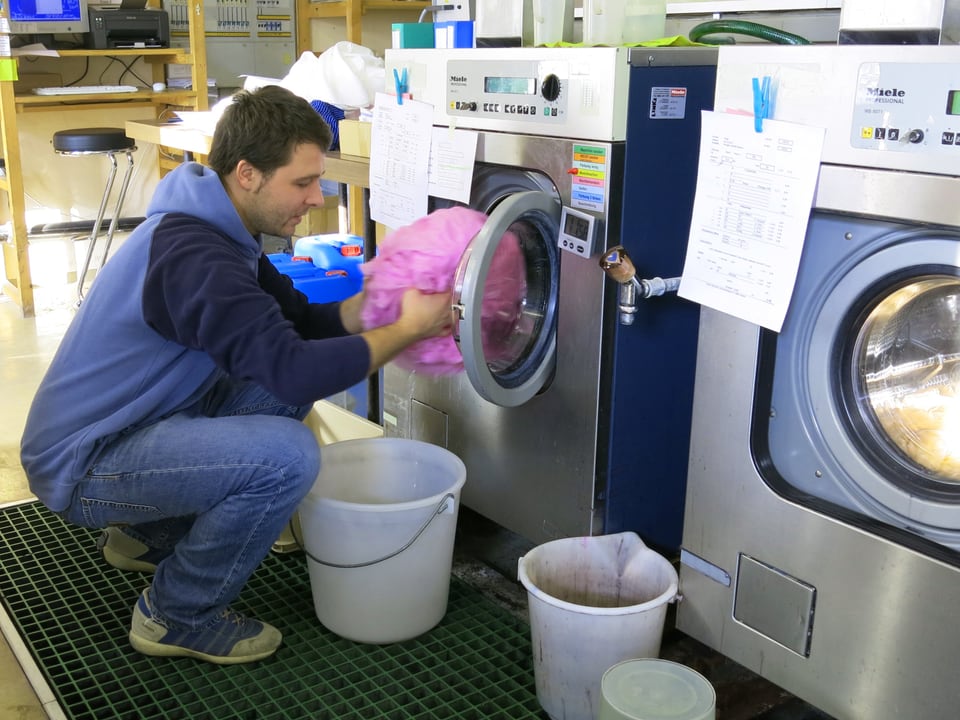 Ein Mann nimmt farbigen Stoff aus einer Waschmaschine. 