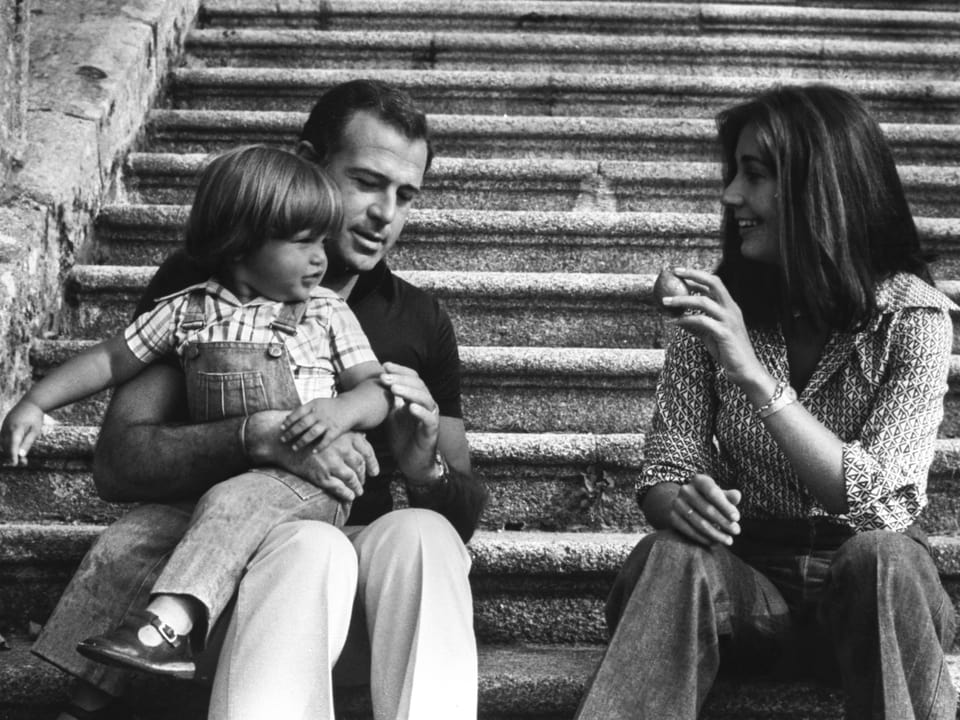 Alfonso de Borbon sitzt auf einer Treppe, seinen Sohn auf den Knien. Neben ihm seine Frau.