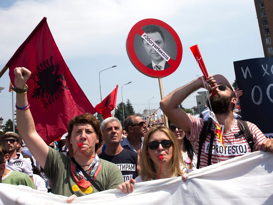 Demonstrierende pfeiffen und halten Fäuste in die Höhe. Im Hintergrund ist der albanische Adler zu sehen.