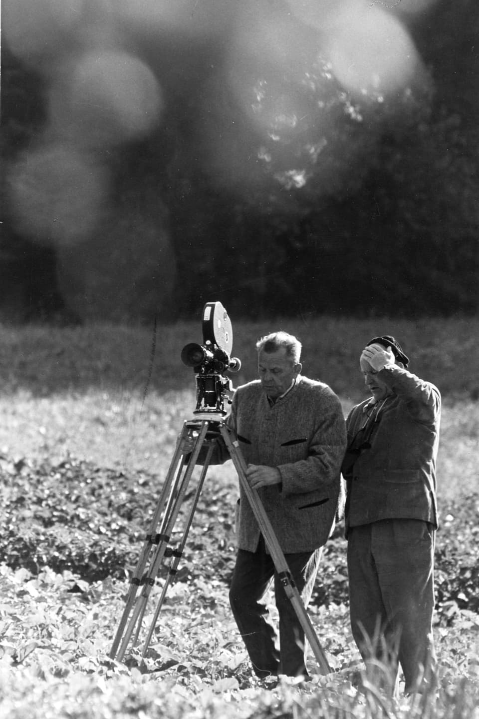 Der Kameramann stellt die Kamera in einem Feld auf Stativ auf. Neben ihm steht Franz Schnyder.