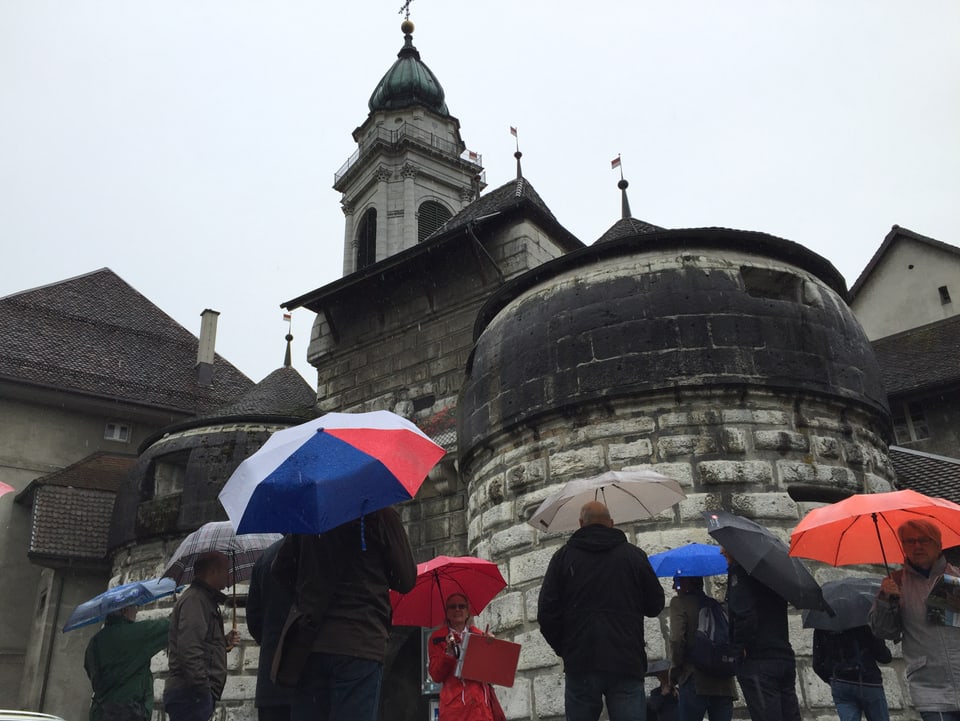 Touristen mit Regenschirmen blicken zum historischen Baseltor, dahinter eine Kathedrale