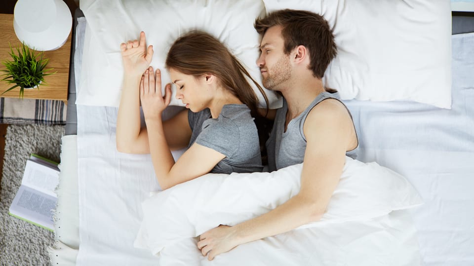 Ein mann kuschelt sich seitlich an eine Frau im Bett.