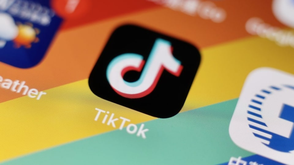 Ein Handy mit Tiktok-Logo drauf. Im Hintergrund sieht man eine China-Flagge.
