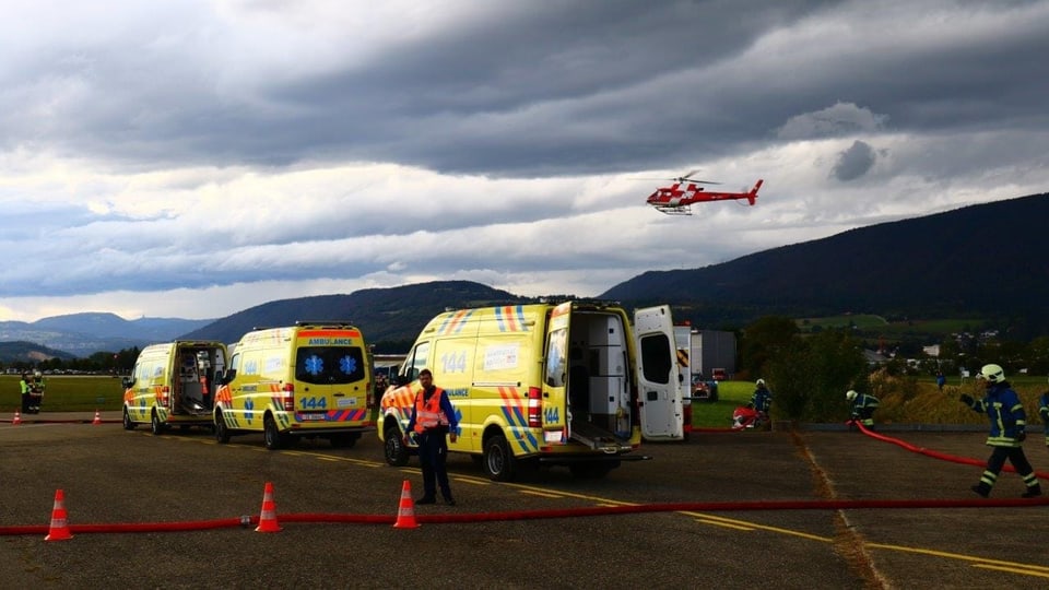 Ambulanzen stehen auf dem Rollfeld, im Hintergrund fliegt ein Rega-Helikopter