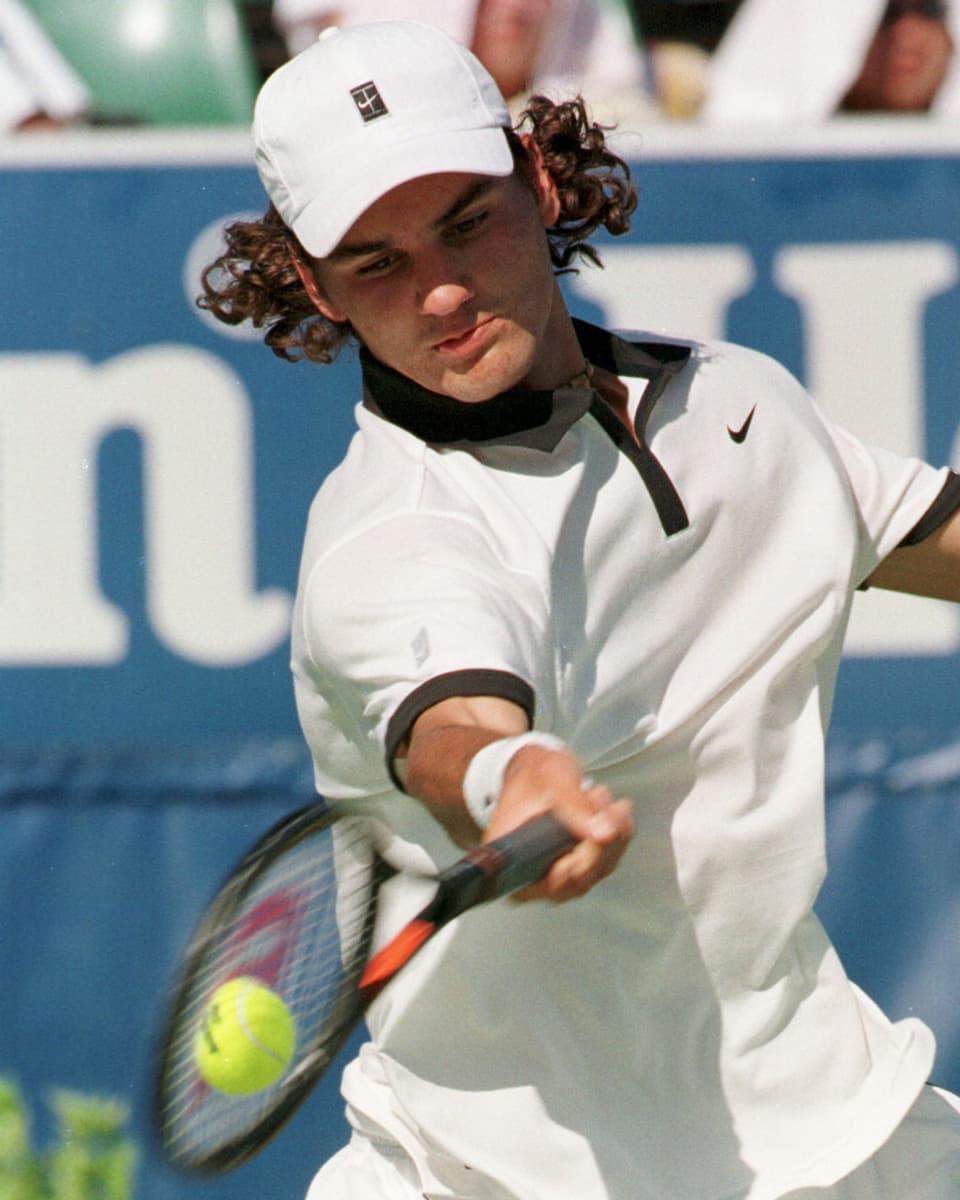 Federer im weissen Shirt mit wehendem Haar schlägt eine Vorhand.