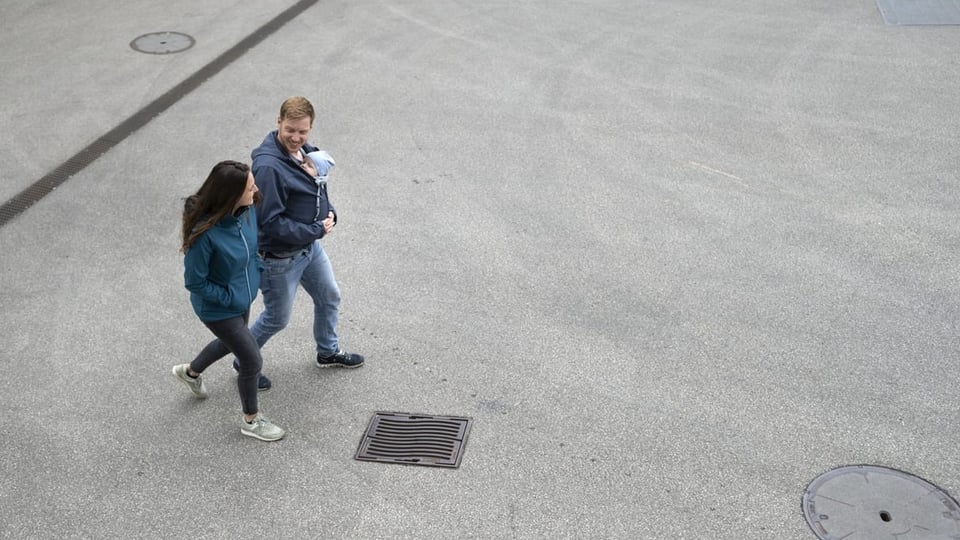 Ein Mann spaziert neben seiner Frau mit seinem Sohn, der in einem Tragetuch eingewickelt ist, spazieren,