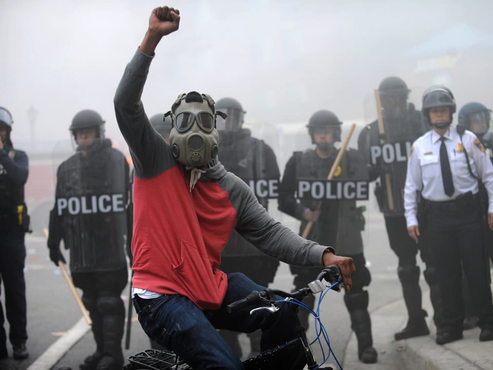 Ein Demonstrant hebt die Siegesfaust auf einem Fahrrad vor einer Reihe Polizisten. 