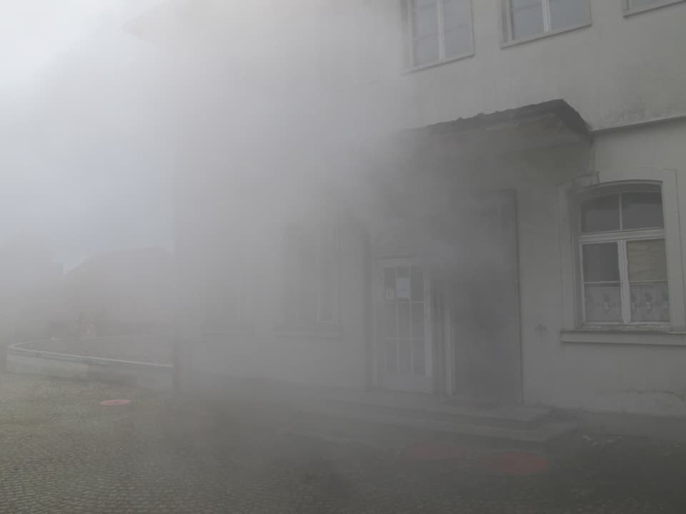 Vor einem Gebäude auf dem Areal wird das Gebiet grosszügig mit Nebel überzogen.