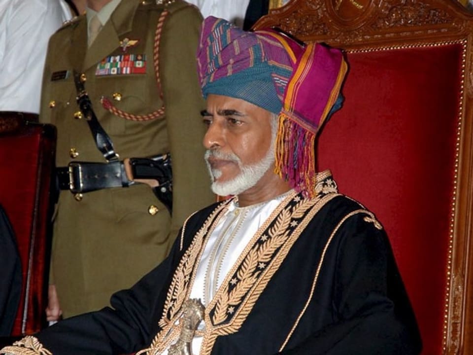 Sultan Kabus mit Turban auf einem roten Thron sitzend.