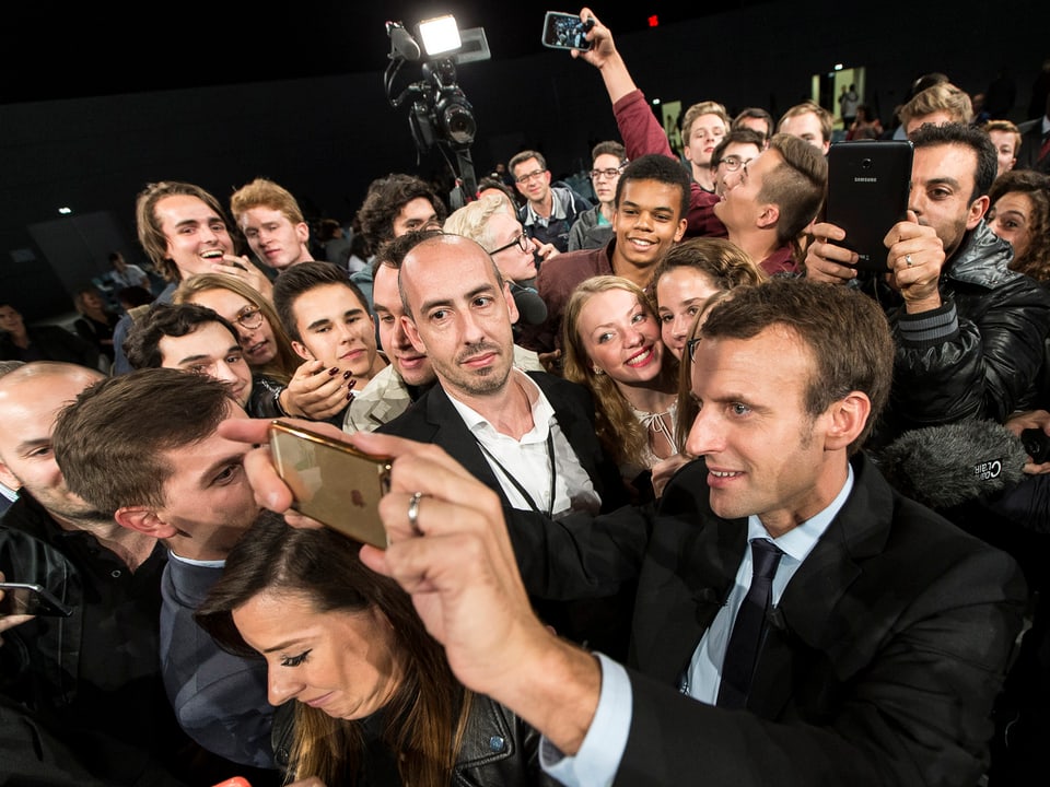 Emmanuel Macron schiesst gemeinsam mit einigen Wählern mit einem Smartphone ein Selfie. 