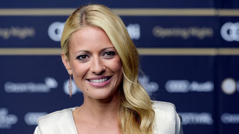 Christa Rigozzi in einem weissen Kleid vor einer Fotowand. 