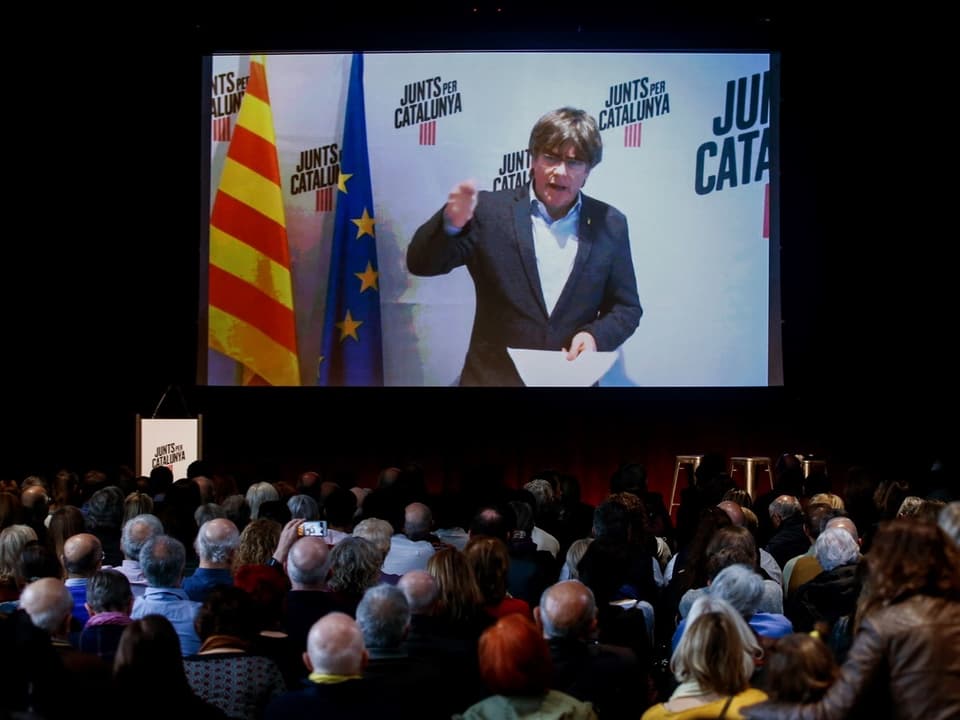 Carles Puigdemont spricht per Videoübertragung zu einem Publikum.