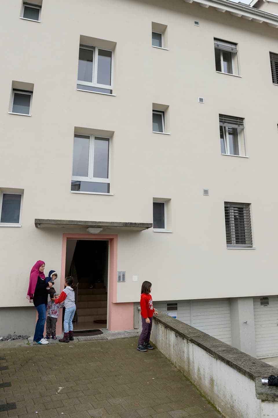 Frau mit Kopftuch und drei Kinder vor dem Eingang in einen Wohnblock