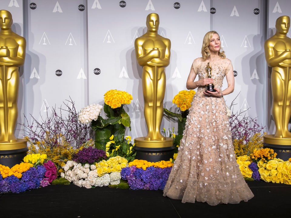 Cate Blanchett steht mit einem Oscar vor übergrossen Oscar-Statuen 
