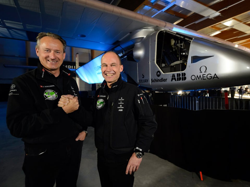 Andre Borschberg und Bertrand Piccard reichen sich die Hand, im Hintergrund die «Solar Impulse 2»