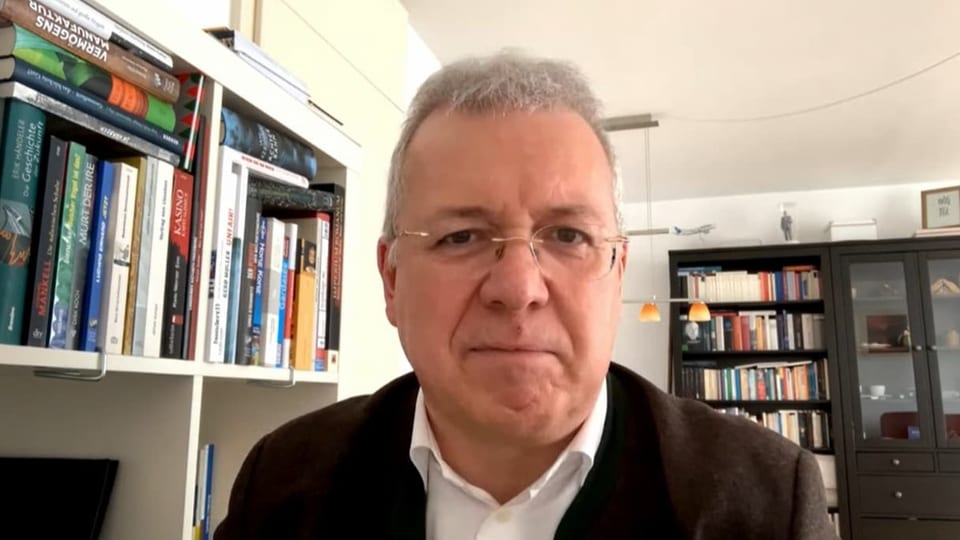 Mann sitzt in Zimmer, dahinter Bücherregale