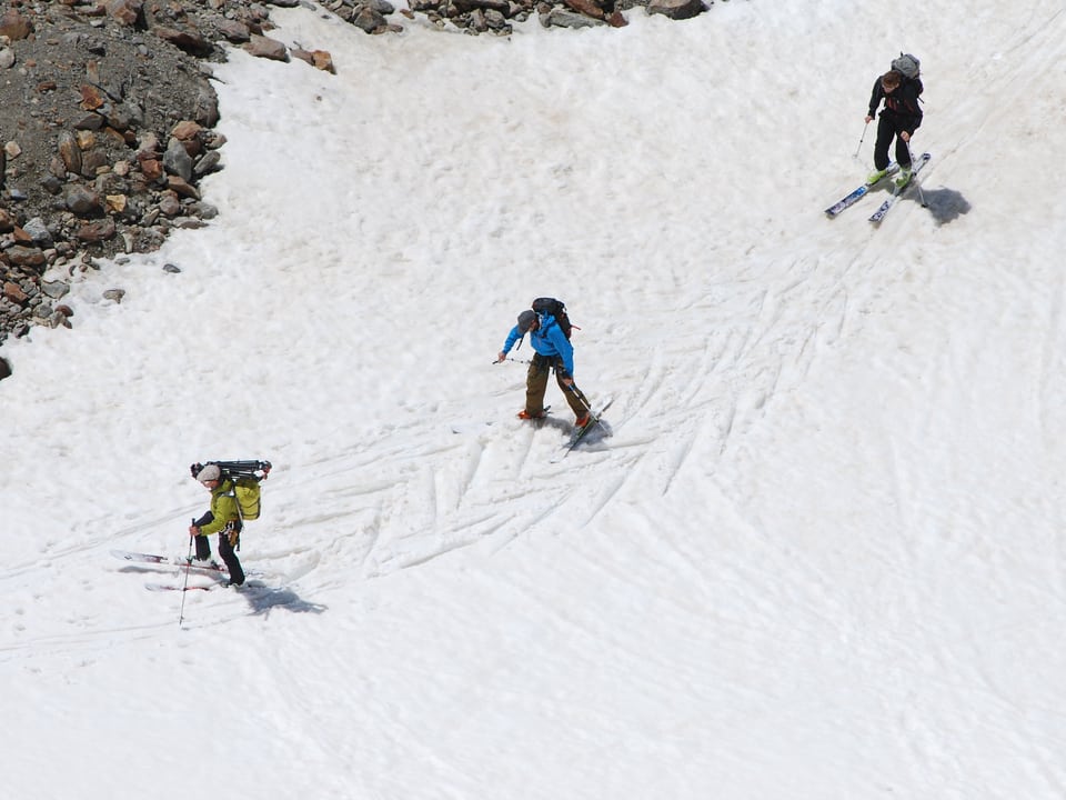 Drei Männer mit steigen mit Skiern das Schneefeld hinauf. 
