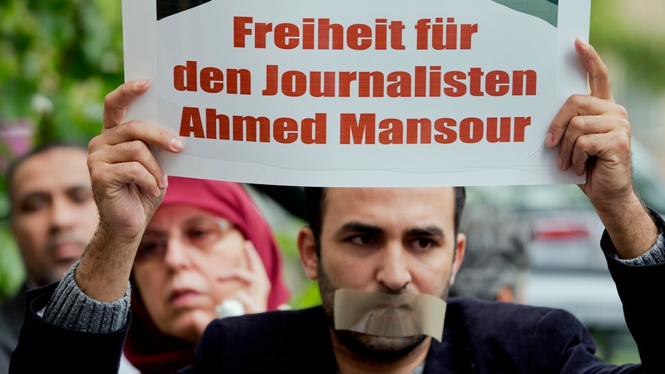 Ein Mann, der sich den Mund zugeklebt hat, hält ein Plakat mit der Aufschrift «Freiheit für den Journalisten Ahmed Mansour»