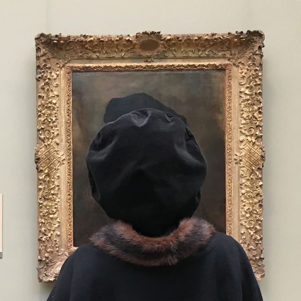 Frau mit schwarzem Hut steht vor einem Gemälde im Museum