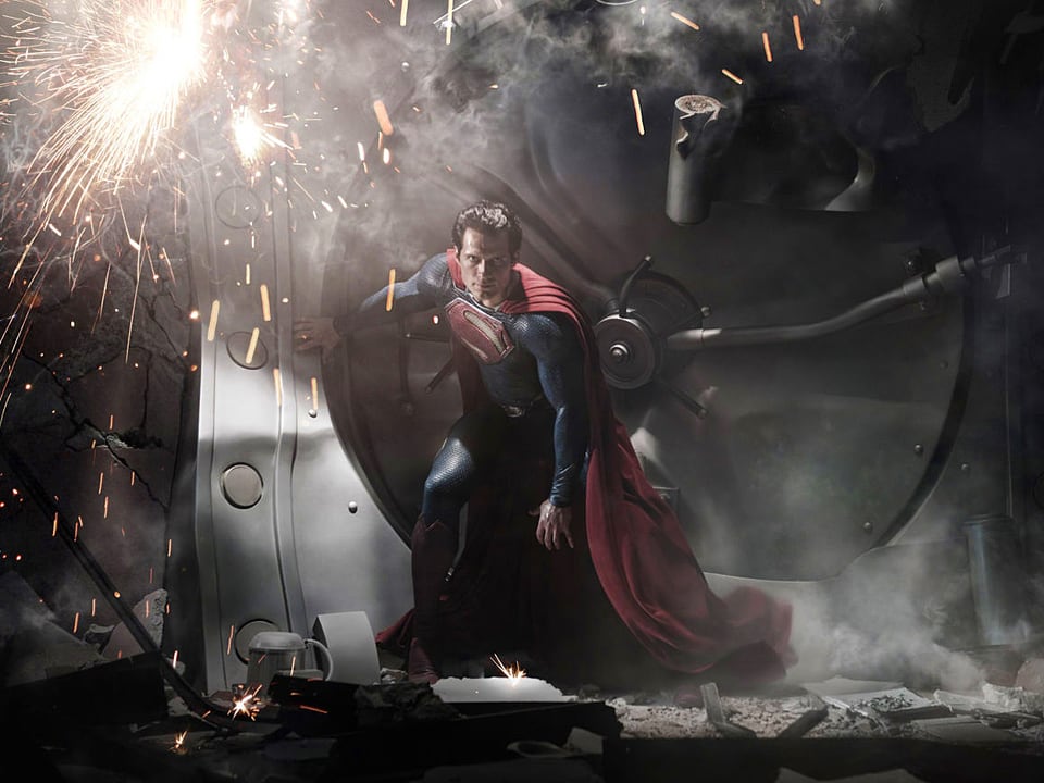 Superman in einer dunklen Halle, in der von oben herab Funken sprühen.
