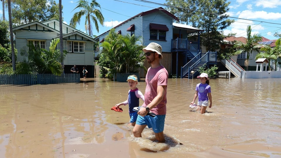 Ein Erwachsener und zwei Kinder schreiten bei Brisbane durch die Fluten.