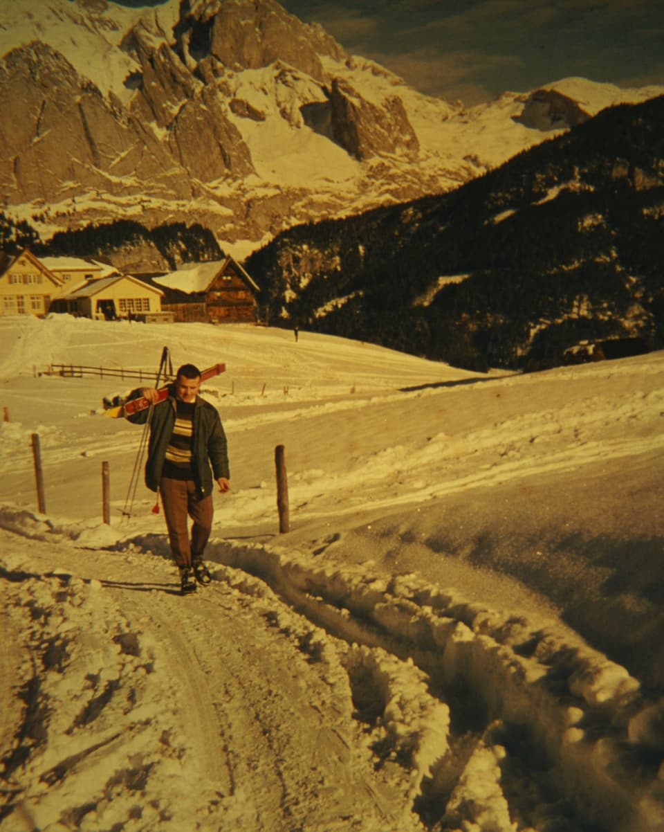Ein Mann geht mit den Skiern auf dem Buckel über einen verschneiten Weg.
