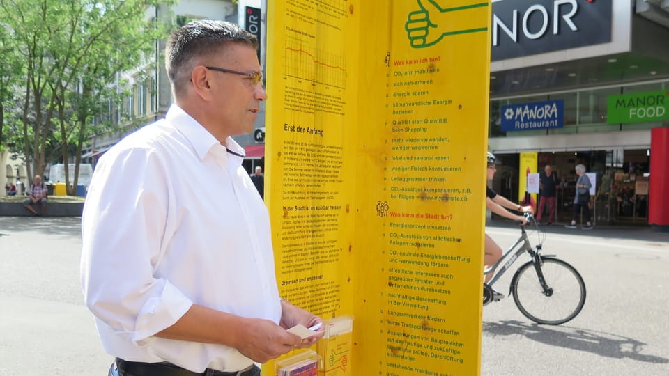 Stadtammann Schneider steht vor Holztafel mit Infos über den Klimawandel. Im Hintergrund sieht man ein Fahrrad.