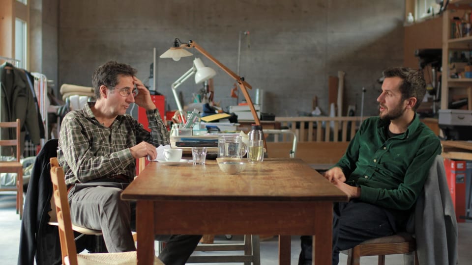 Eine Filmszene in der ein Vater und ein Sohn an einem Tisch sitzen und miteinander reden. 