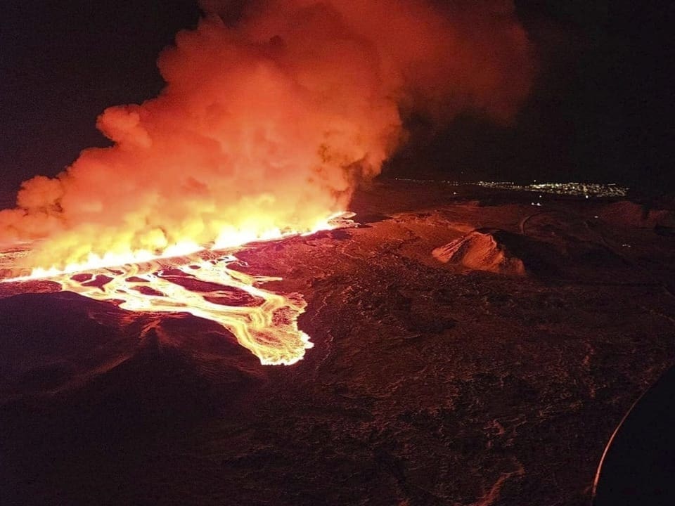 Eine grosse Rauchvolke steigt über einer von Lava begossenen Landschaft auf.