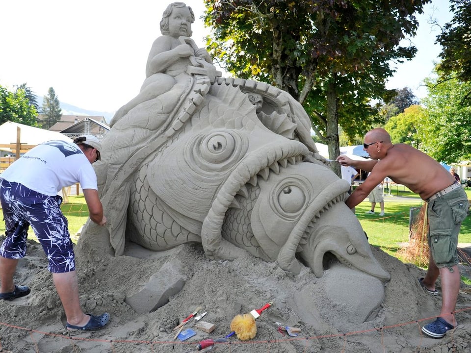 Zwei Künstler arbeiten an einer Sandfigur.