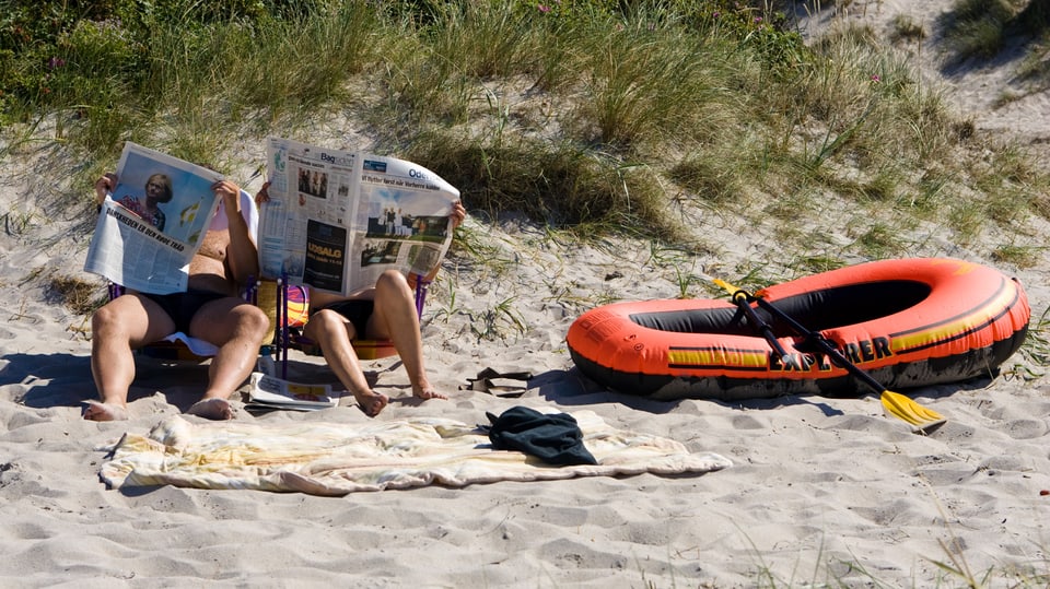 Zwei Menschen am Strand, die Zeitung lesen.