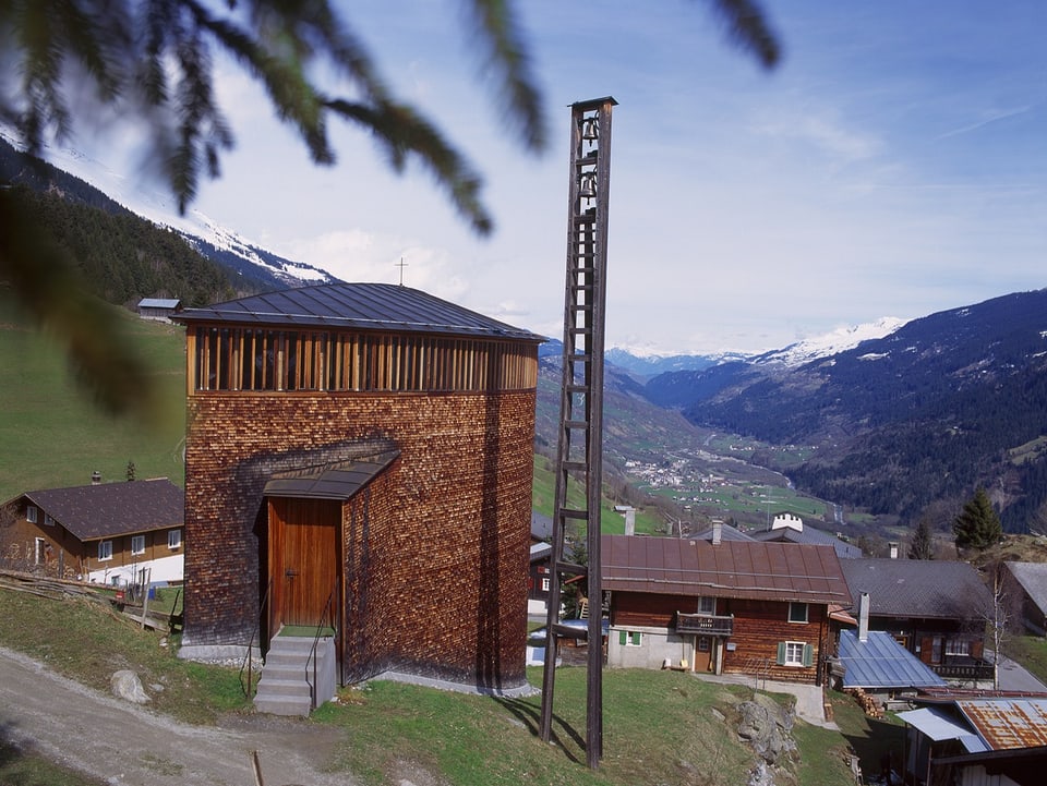 Blick auf auf Holzgebäude und Mast im Vordergrund vor Alpental im Hintergrund