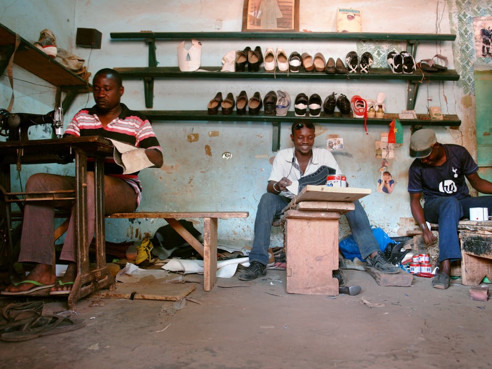 Drei schwarze Männer in einer sehr einfachen Schuhwerkstatt