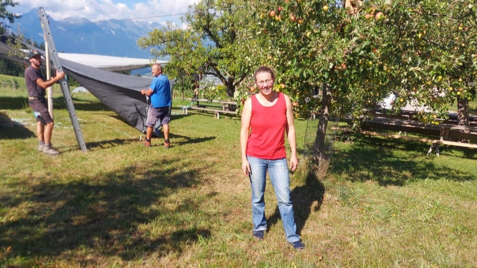 Eine Frau steht auf einer Wiese, auf der Festbänke aufgestellt sind.