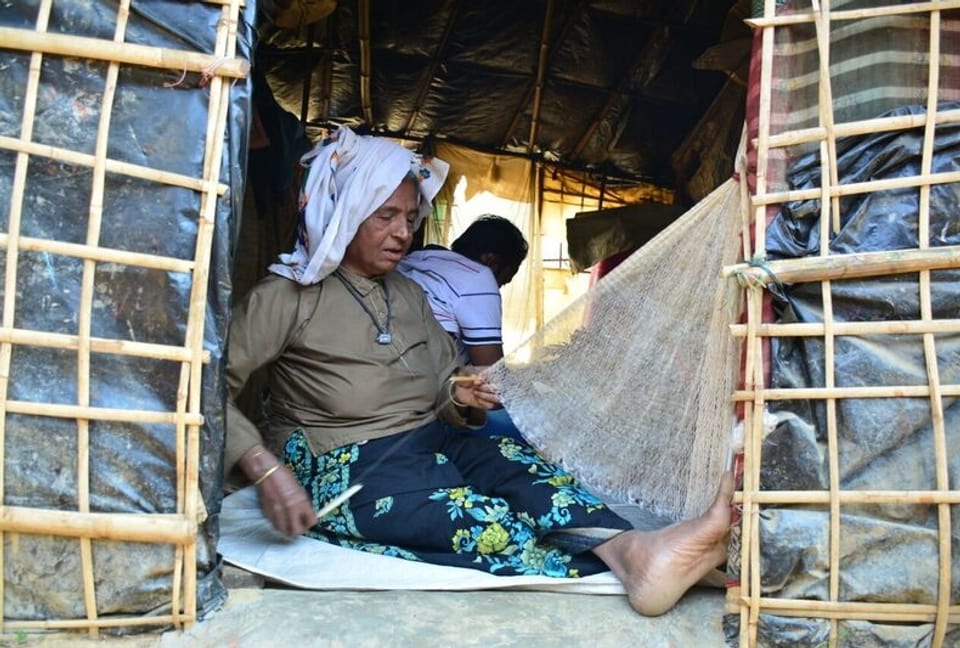 Ältere Frau sitzt in einfacher Behausung