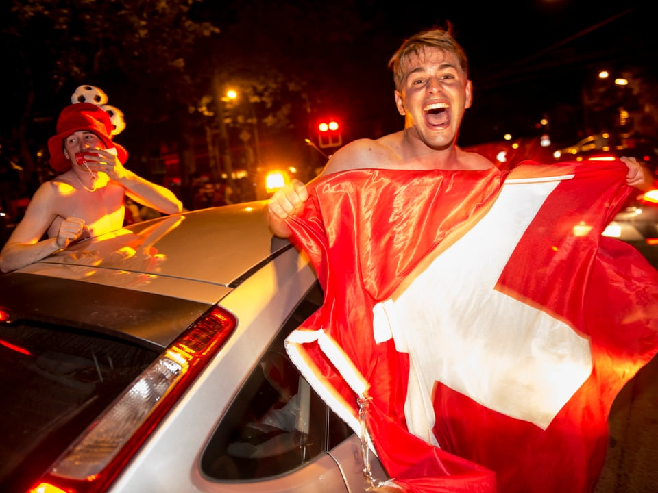 Fan mit Schweizer-Flagge ragt aus Autofenster.